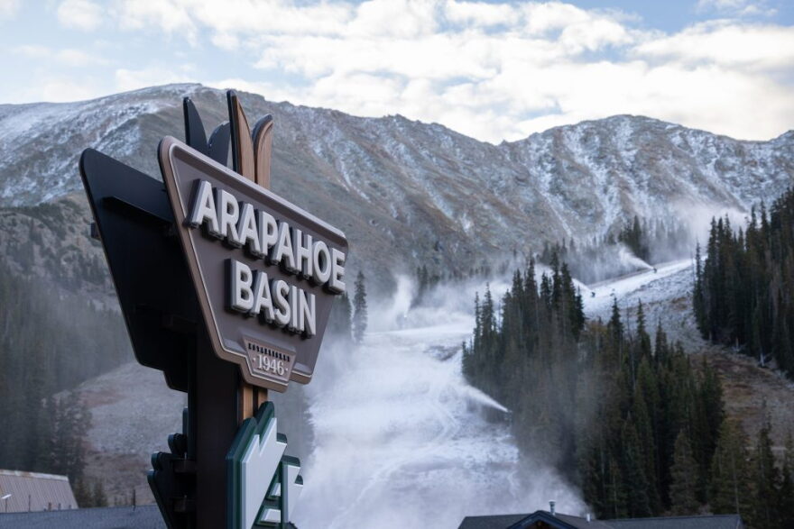 The Arapahoe Basin Ski Area sign in front of a mountain that's beginning to be covered in snow.