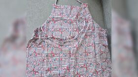 An apron with a strawberry and teapot pattern against a gray background.