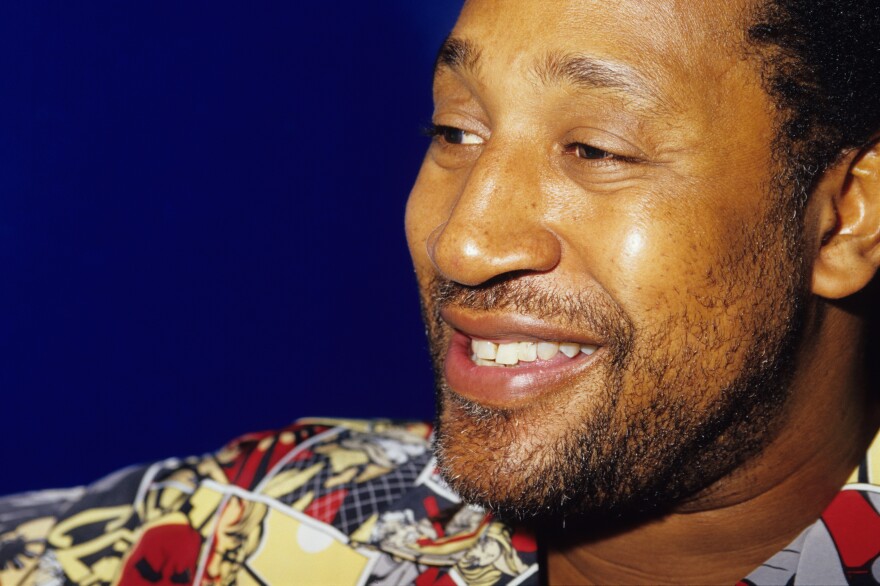 A close-up of a smiling man with a closely cropped beared and a colorful shirt.