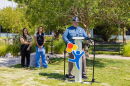 A man in a state trooper uniform stands at a podium, addressing an audience. Two women stand behind him, looking on.