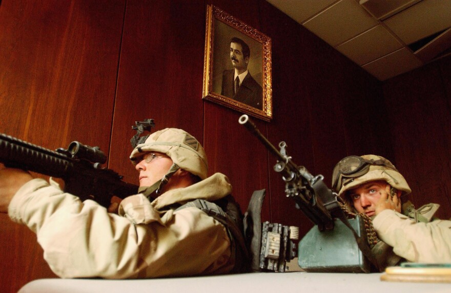 U.S. soldiers take cover near a portrait of Saddam Hussein while conducting a sweep of the VIP terminal of Baghdad International Airport on April 4, 2003.