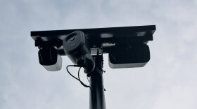 A Flock camera with a solar panel sits on a pole.