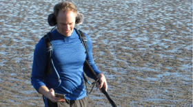 Chet Udell looks at his flashing metronome as he carries a boom microphone recording his footfalls and other environmental sound while he jogged around Newport, Ore., on Jan. 19, 2026.
