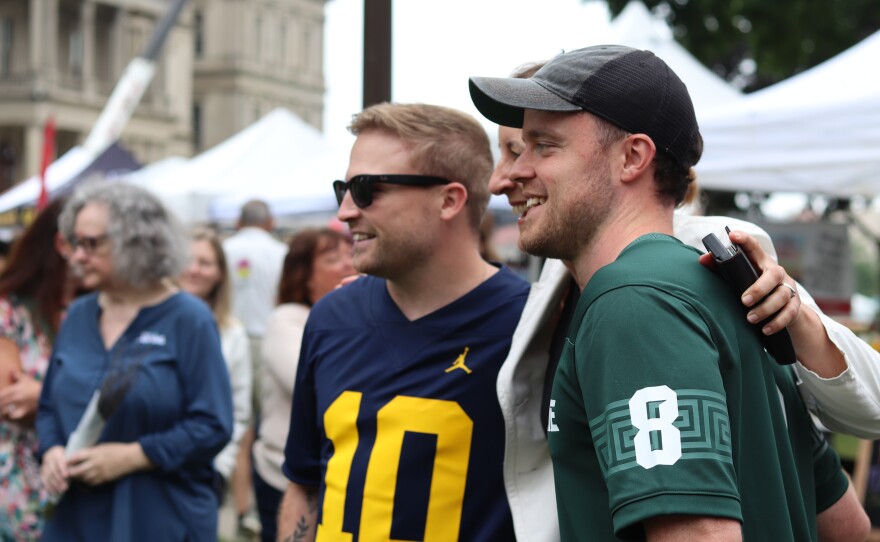 Photos of Josh and Jace, two young British men, taking photos with fans and mascots. The two are wearing a blue University of Michigan and a green Michigan State University jersey respectively.