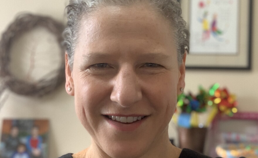 A smiling woman with short grey hair is wearing a dark blue scrub top.