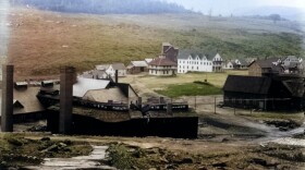 An old timey photo of a village center surrounded by largely deforested hills. At least a dozen buildings are visible.