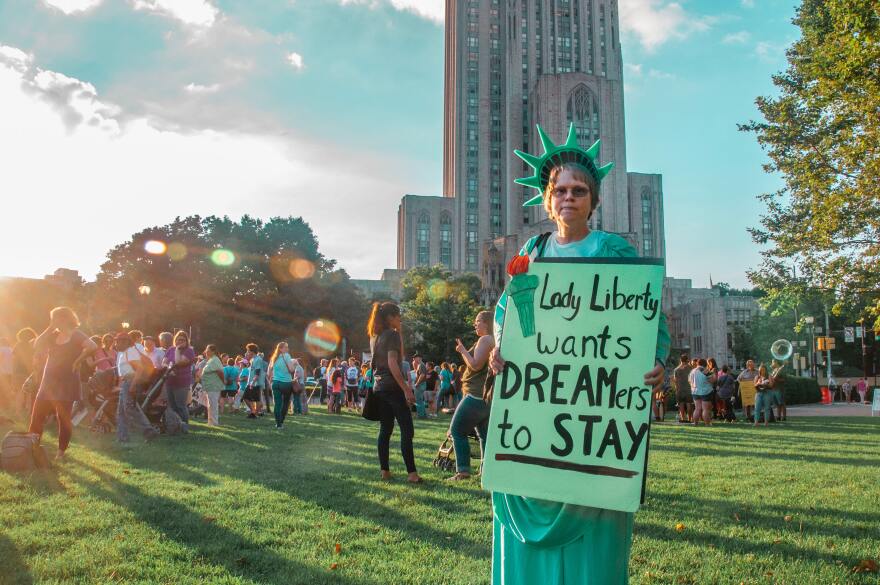 A woman dressed as the Statue of Liberty holds a sign that says "Lady Liberty wants DREAMers to stay."