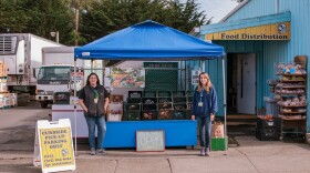 Two women standing next to a pop-up tent displaying boxes of food.