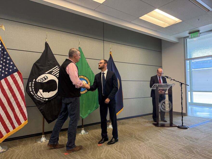 Two men shake hands in front of a row of flags