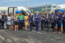 A group of people in dress clothes cut a ribbon in front of two transit vans