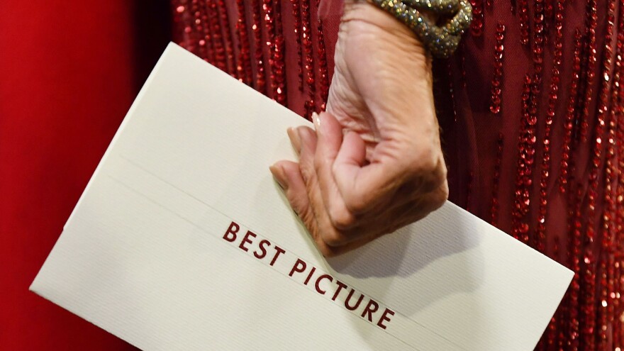 A close-up of a woman's hand holding an envelope that reads "Best Picture."