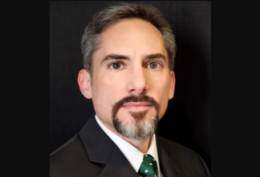 Head shot of man with a goatee and wearing a black suit with green spotted tie 
