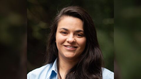 Stella Mayerhoff smiles at the camera. She has long, brown hair and is wearing a light blue dress shirt.