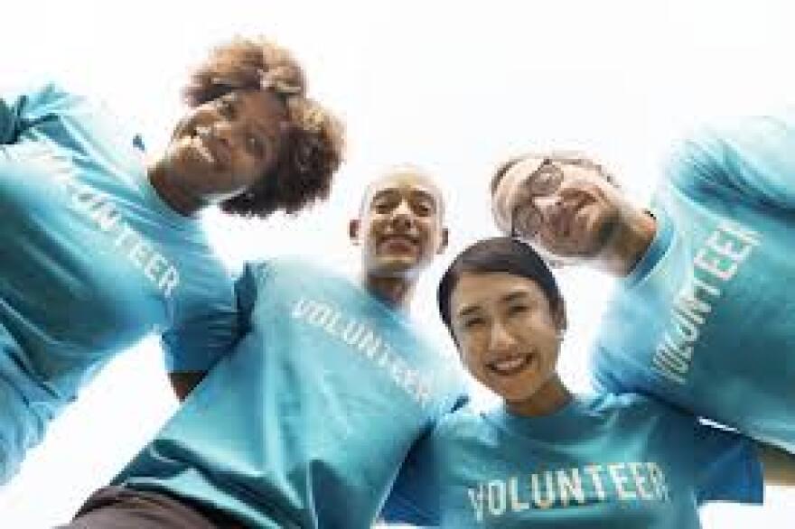 Four people smiling with a shirt that reads volunteer.