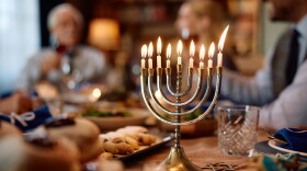 Lit candles in menorah during Hanukkah celebration. The family is in the background.