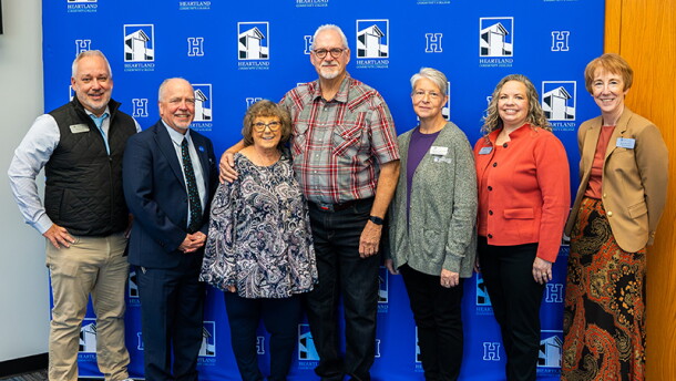 A group of adults, including Keith Cornille and Jim Davis, stand together for a photo in front of a blue backdrop. 