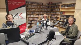 Three people smile at the camera in a radio studio.