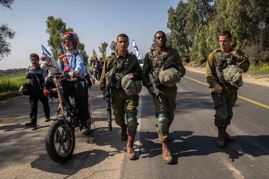 An Israeli activist dressed as a clown rides an electric bike alongside Israeli soldiers accompanying families of the hostages and supporters near the start of the four-day march to Jerusalem on Feb. 28. The activist, who goes by the name "Hashoteret Az-Oolay," regularly attends demonstrations for a variety of issues across Israel.