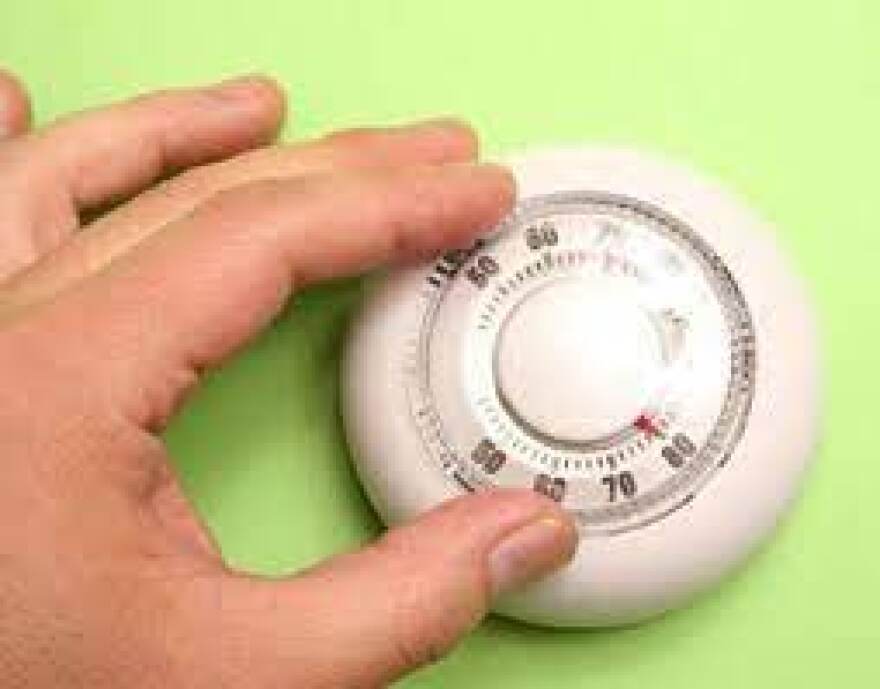 A hand turning down a thermostat