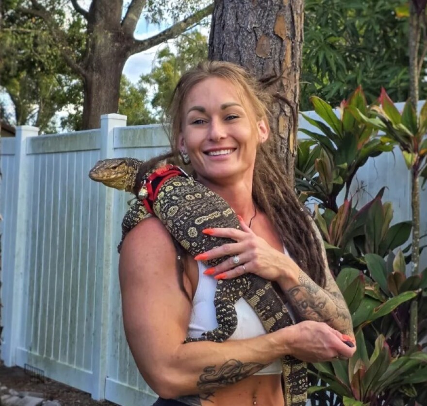 Woman with tattoos holds lizard on chest