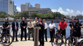 multiple law enforcement officers stand side by side in front of a river. some have bicycles with thick tires and also helmets