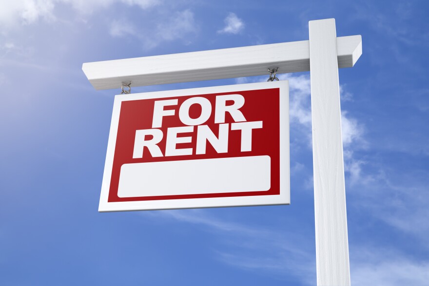 A red "for rent" sign against a blue sky.