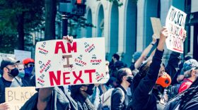 A person protesting the murder of unarmed 19 year-old Christian Hall by Pennsylvania state police in 2021 holds up a handwritten sign saying, "AM I NEXT?"