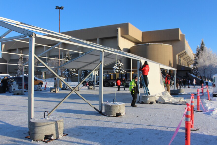 People pull canvas over a steel frame in front of a large brown building