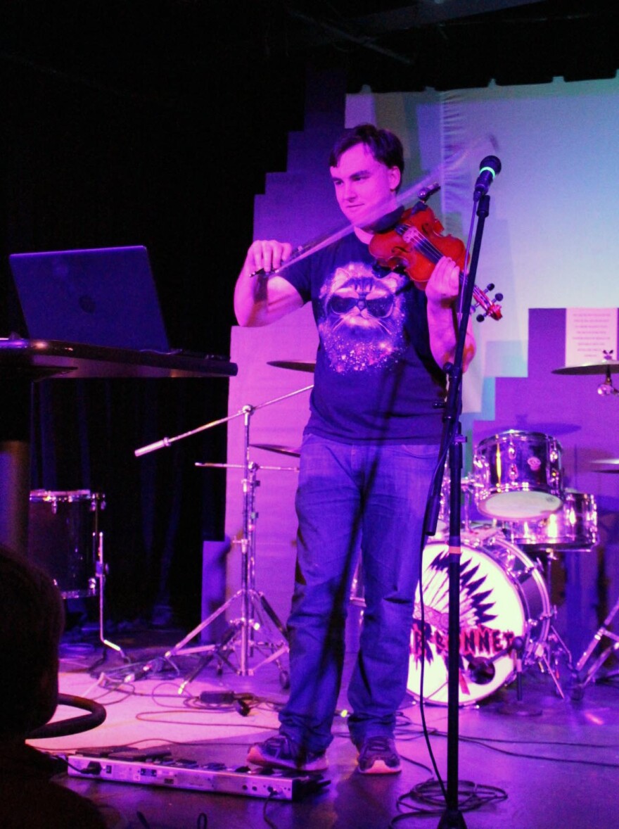 Man playing a violin with a lap top in front of him