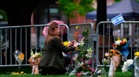 A woman places a bouquet of flowers along a guardrail where other flowers have been left.