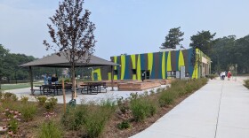A photo taken outside shows people sitting outside and a yellow, green and brown striped building.