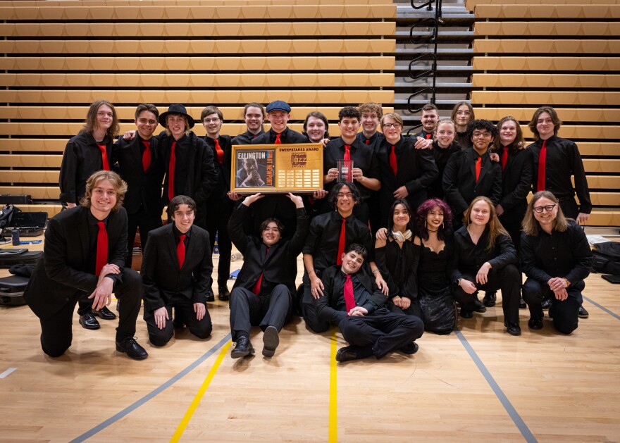 A group of teenagers dressed in black wearing red ties. One of the teenagers is seated on the floor holding up a plaque.