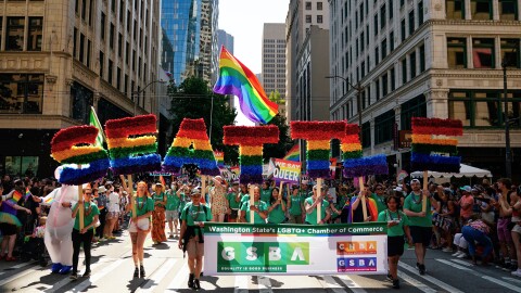 People march in a Pride parade holding rainbow letters that read Seattle.