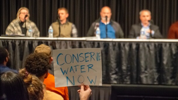 One attendee holds up a sign that says "conserve water now" in front of the panel of Google representatives on Thursday. One representative outlined Google's planned requests for further wetland mitigation credits as well as a plan to relocate Adams Ditch on the property.
