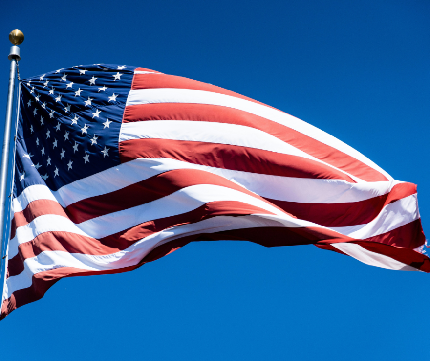 an American flag hanging from a flagpole against an open sky.
