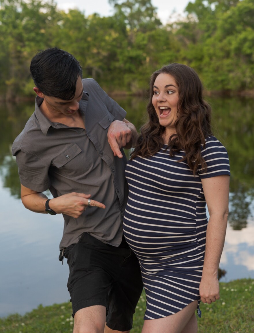 a man points to his wife's pregnant belly. 
