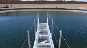 A think metal platform stretches over a wide, round manmade pond full of blue water