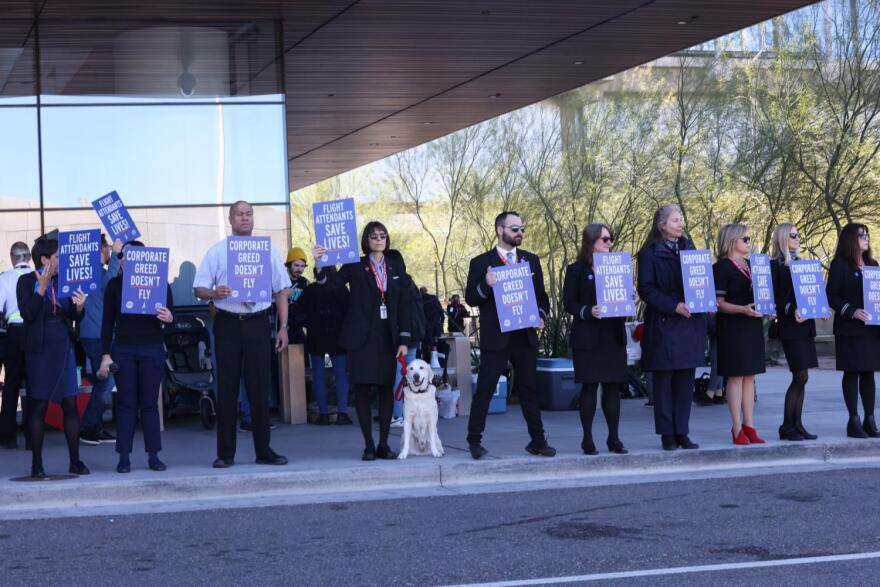 People holding signs line up outside with dog in middle