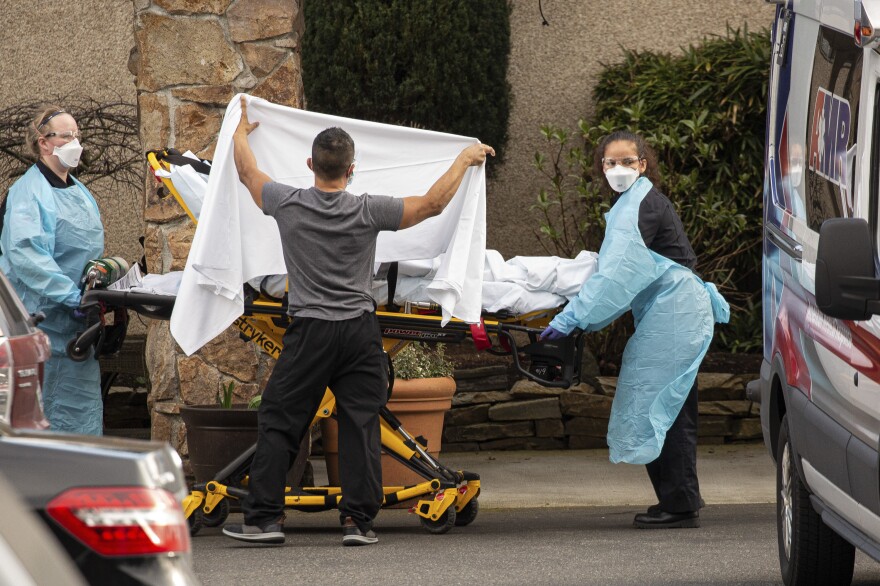 Health care workers bring a patient into an ambulance at Life Care Center in Kirkland, Wash. Two deceased residents of the eldercare facility had posthumous diagnoses of COVID-19, the disease caused by the new coronavirus.