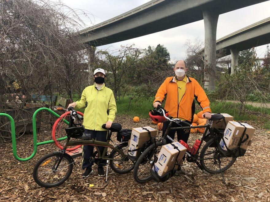 Image 1: Miki and Jon in brightly colored jackets posed with their bikes, produce boxes strapped and ready to go. Image 2: Cream and black toned rooster standing near a metal fence. Image 3: Hand-painted wooden Veggielution directional sign. 