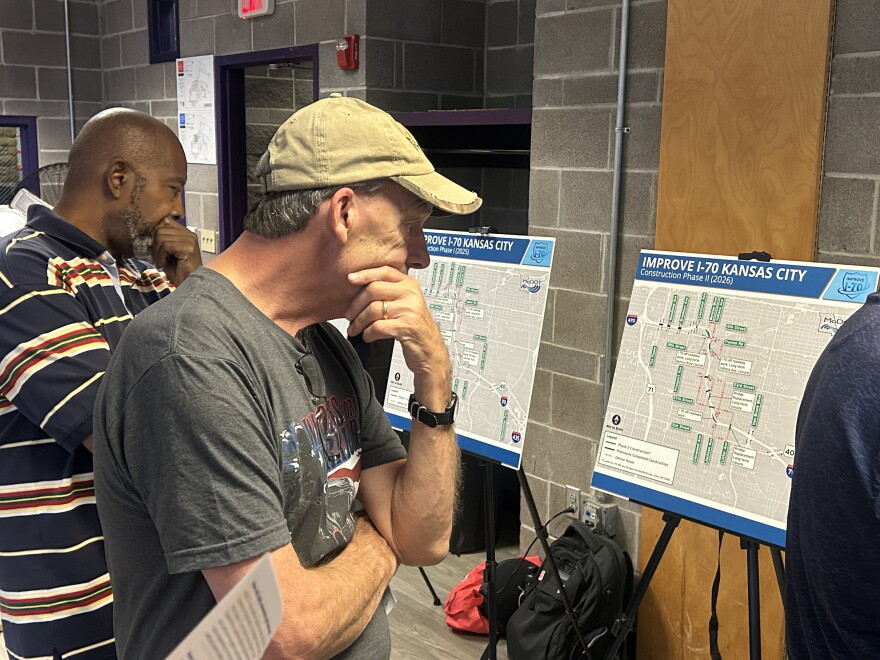A man wearing a baseball cap looks over a map sitting on an easel. 