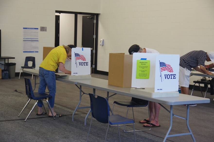a man and woman fill in a ballot behind a screen that includes an American flag