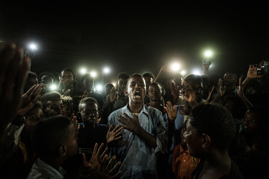 People chant slogans as a young man recites a poem, illuminated by mobile phones, at a protest in Khartoum, Sudan in June 2019.