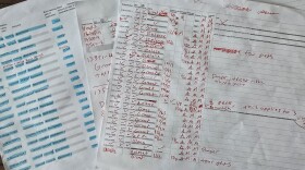 A photograph of overlapping documents laid on a dark wood surface. The bottom document appears to be a printed spreadsheet tracking immigration bond hearing outcomes, with columns including docket numbers, dates, bond amounts, and results — many cells show "Bond denied" highlighted in blue. The top document is a densely annotated printed form, heavily marked up in red handwriting. Handwritten notes include words and phrases such as "Grant," "Release," "Denied,"  and various dates and acronyms. The documents arerelated to immigration detention bond hearings, compiled by a journalist collecting data on court documents.