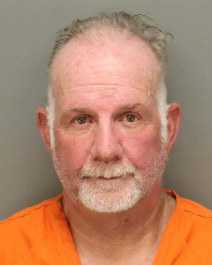 A man with grey hair and beard wearing an orange jumpsuit. 