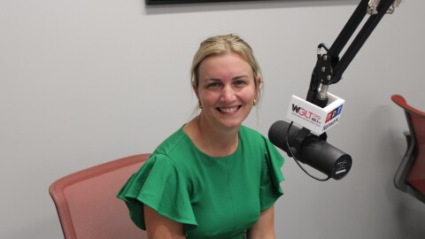 A woman in a green dress sits in front of a microphone, smiling 