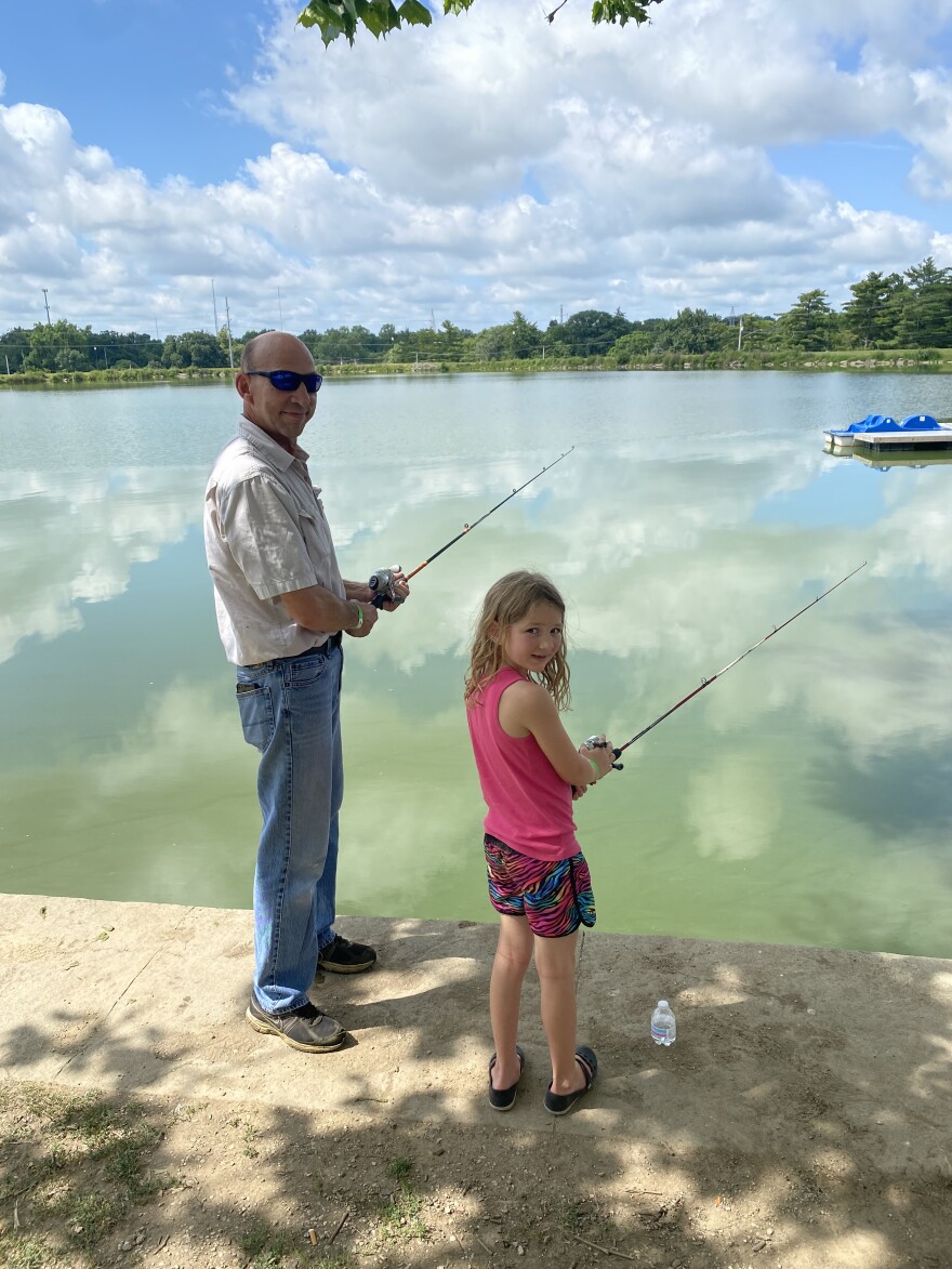 A man fishes with his granddaughter at a lake