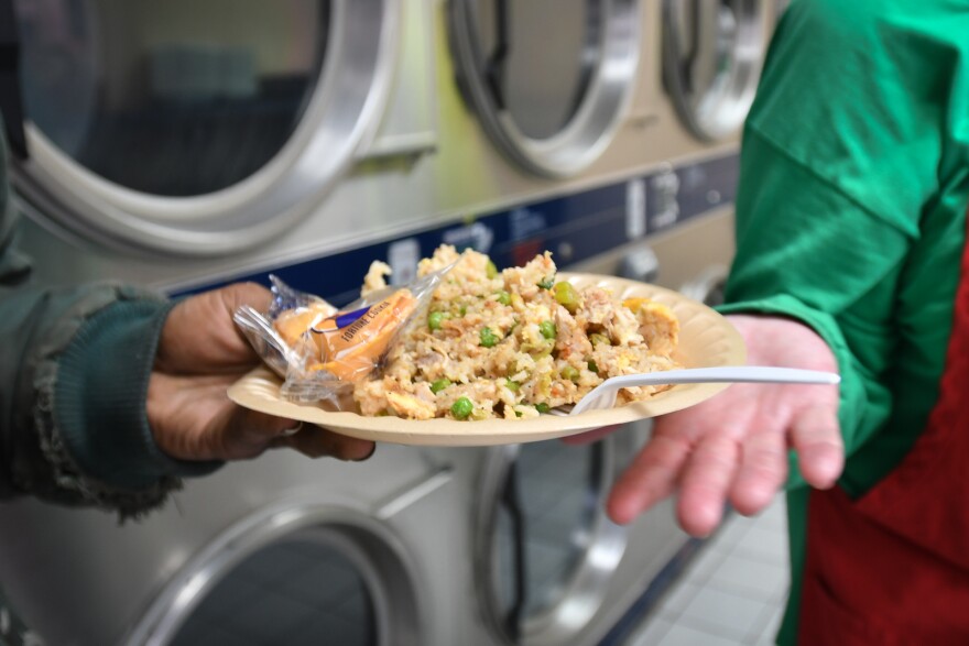 One hand is seen handing off a plate of fried rice to a person holding the plate. Behind them are rows of washing machines.