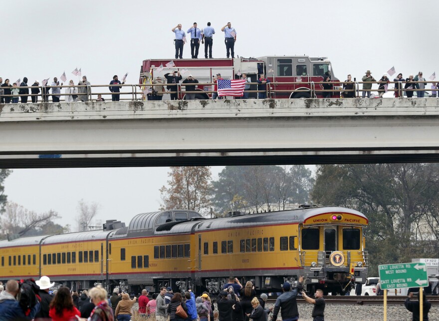 Firefighters stand on their truck and salute with other attendants on an overpass as the train carrying the body of former president George H.W. Bush, the Union Pacific Locomotive 4141, travels past on the way to Bush's final internment Dec. 6, 2018.