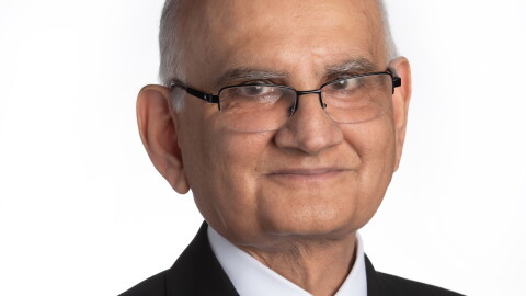 An older man wearing glasses,  poses for a professional headshot against a white background.